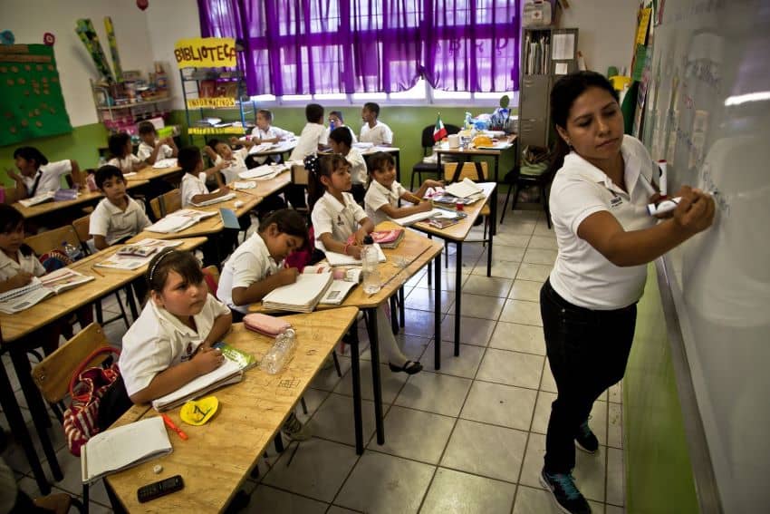 A teacher stands in front of a classroom of students in a Mexican school.