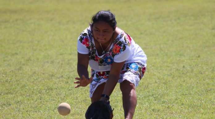 A Maya softball player wearing a traditional huipil pitches the ball.
