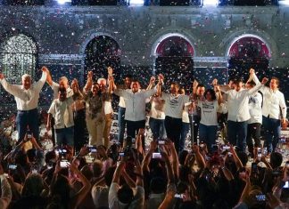 Morena gubernatorial candidate Javier May holds hands on stage with his campaign team, as confetti rains down.