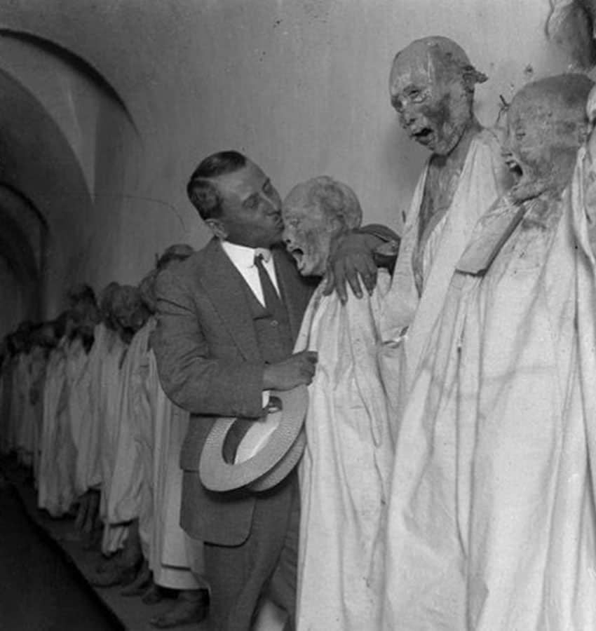 Old black and white photo of man kissing a mummy on display