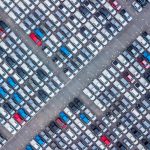 An aerial view of dozens of rows of new cars in a storage lot, ready for export