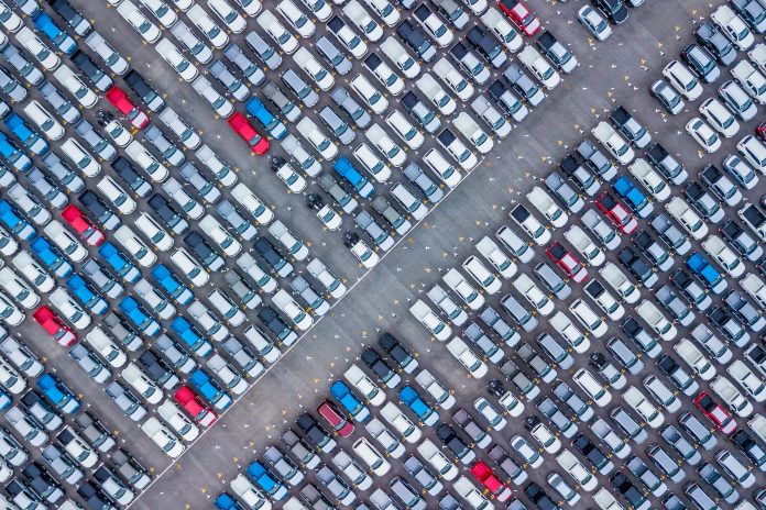 An aerial view of dozens of rows of new cars in a storage lot, ready for export