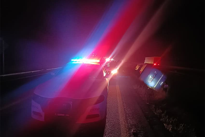 Police car with flashing lights on with overturned passenger bus in the background and to the right