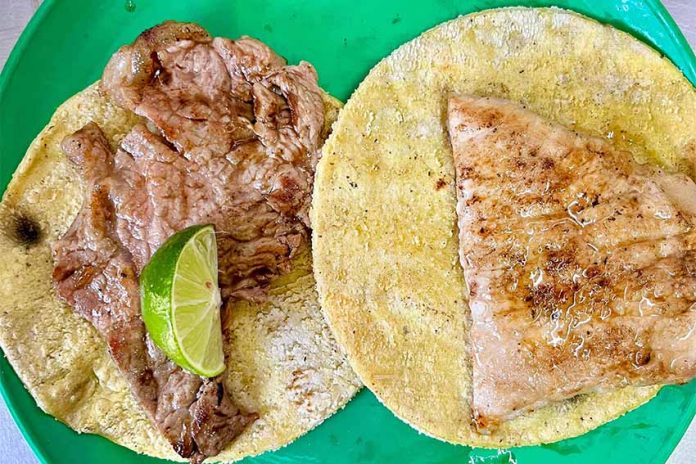 Two tortillas with meat on top, presented on a green plate and with a lime wedge